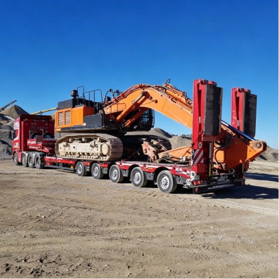 Heavy-duty lowbed trailer transporting excavators across rugged mountain terrain